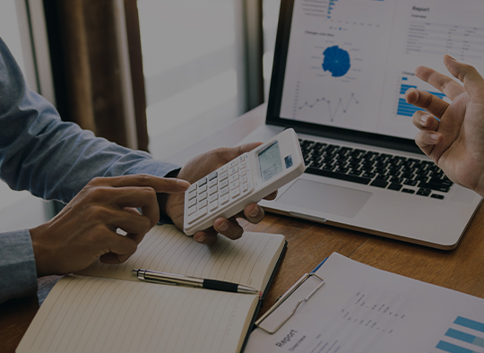 Dos personas utilizando una calculadora y revisando informes financieros en una oficina.